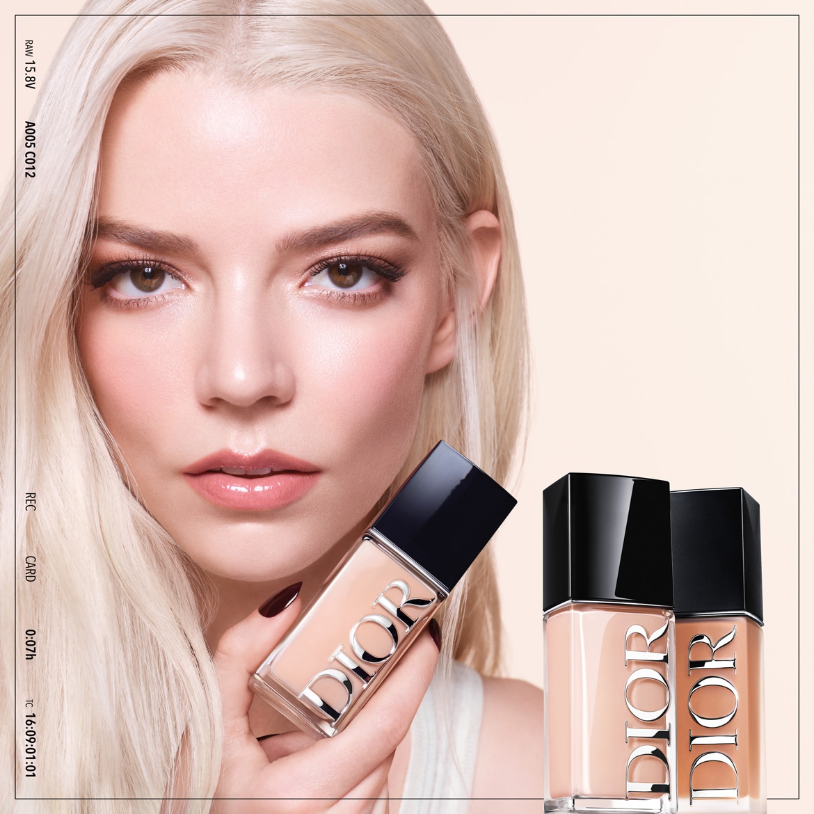 Blondýna s bezchybnou pletí drží v ruce lahvičku make-upu Dior s černým víčkem, v pozadí jsou vidět další dvě lahvičky v různých odstínech.