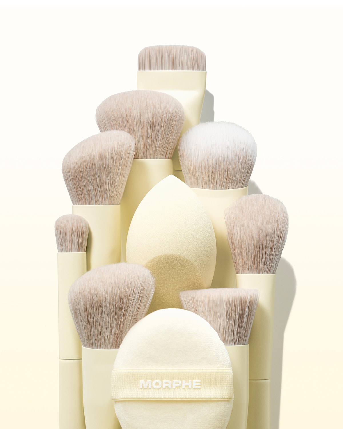 Sada štětců Morphe v krémových barvách s různými tvary a velikostmi štětin, doplněná o houbičku na make-up a pudřenku s logem Morphe.