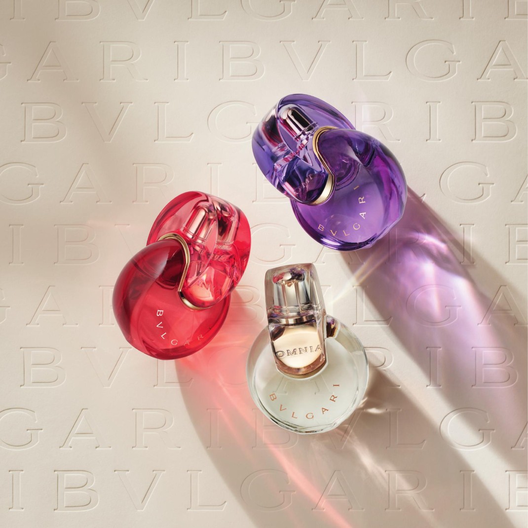 Tři parfémy Bvlgari Omnia v odstínech červené, fialové a čiré, s logem Bvlgari vyraženým na pozadí, vytvářejí elegantní a luxusní dojem.
