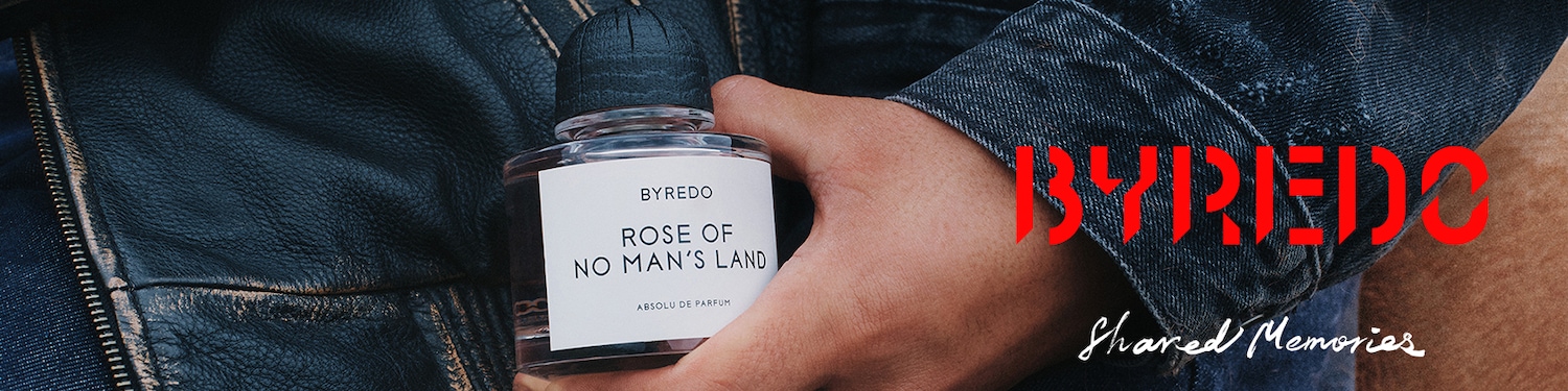 Detailní záběr na parfém Byredo Rose of No Man's Land s dřevěným víčkem, držený v ruce, s koženou bundou v pozadí a nápisem Byredo Shared Memories.