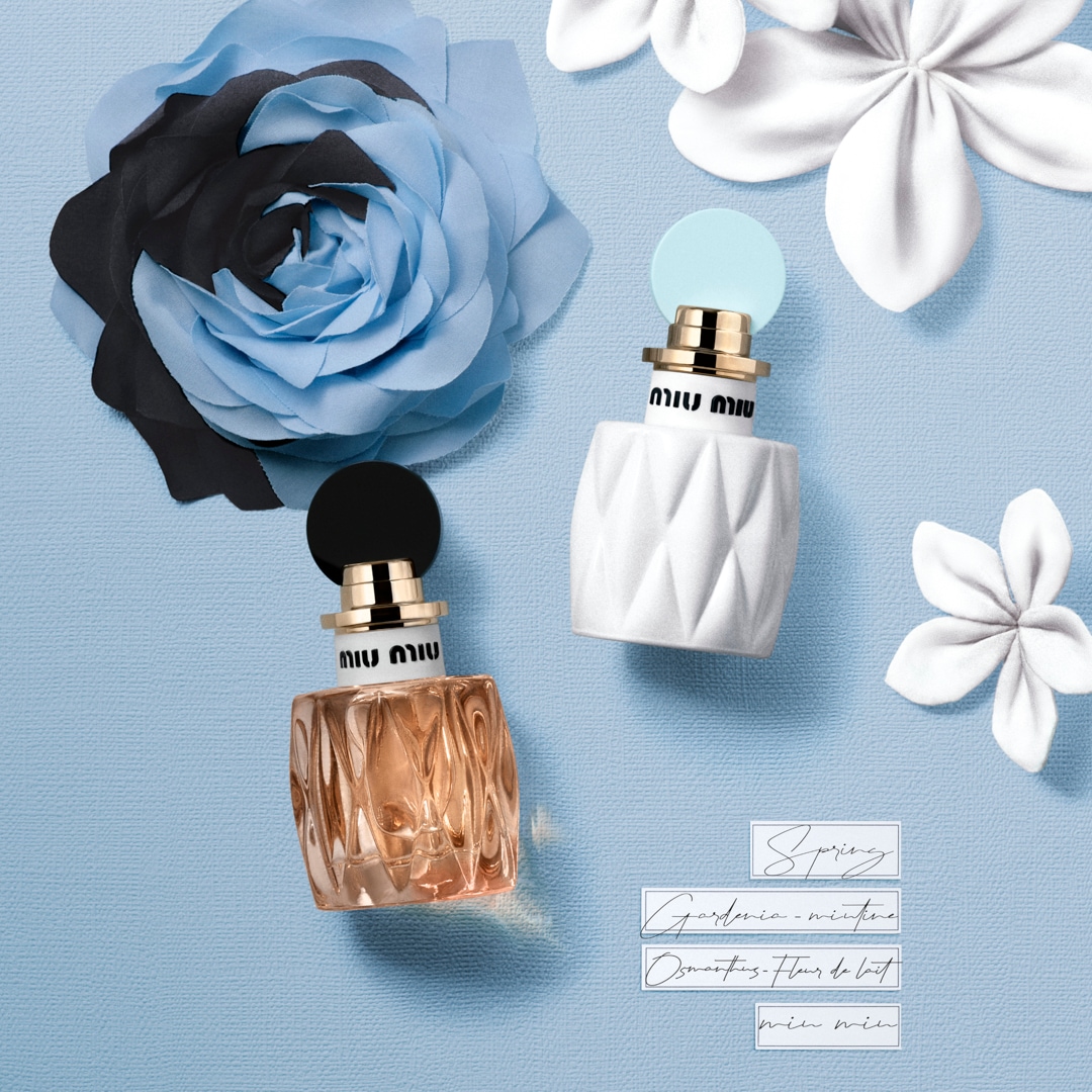 Dva flakony parfému Miu Miu, jeden s bílým a druhý s hnědým obalem, leží na světle modrém pozadí s květinami a textem "Spring Gardenia-minine Osmanthus Fleur de lait min in".